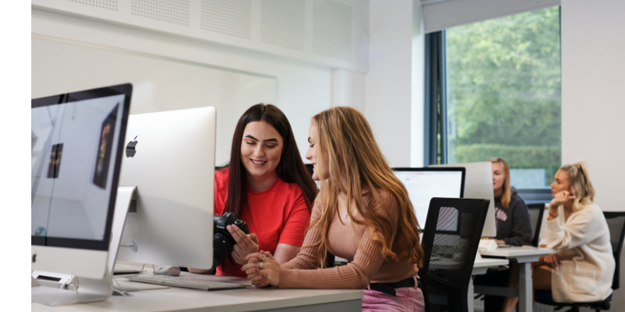 Students sat by a computer, looking at a digital camera