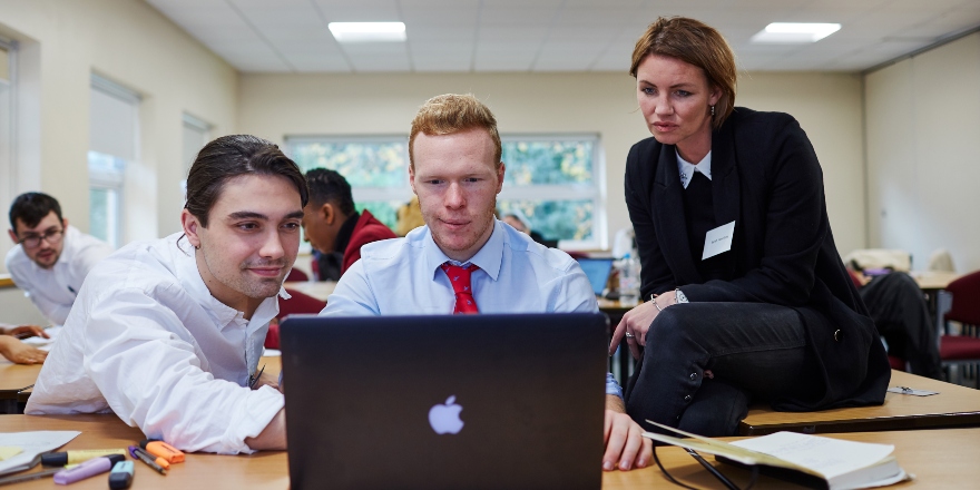 From left to right: male points at laptop screen, with male in red tie and woman in suit 