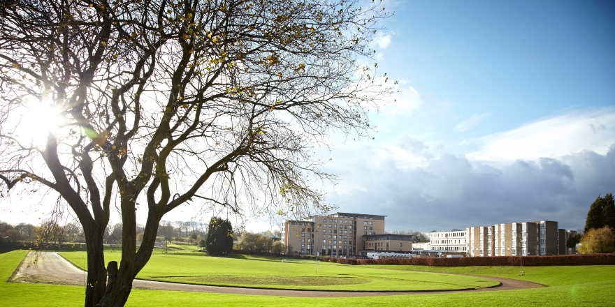 Green campus shot of Leeds Trinity University, with running track and campus buildings